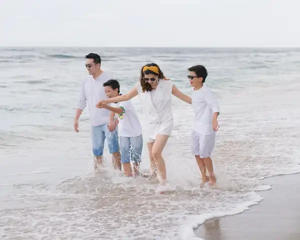 suami istiri dan kedua anak bermain di pinggir pantai menggunakan baju putih, konsep foto untuk paket wisata lombok